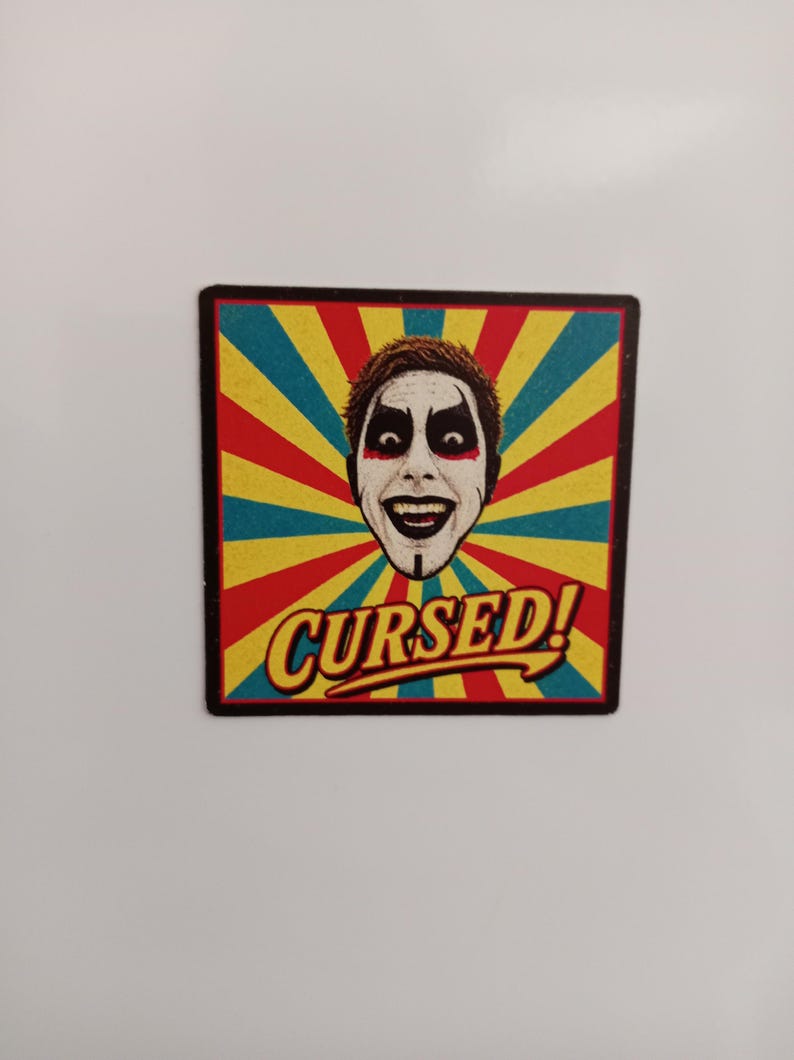 Peut inclure: Un aimant carr&eacute; pr&eacute;sentant une illustration graphique d'une personne avec du maquillage blanc, des yeux maquill&eacute;s de noir et un large sourire. Le fond se compose de rayons de soleil rouges, jaunes et bleu sarcelle. Le mot CURSED! est &eacute;crit en jaune.