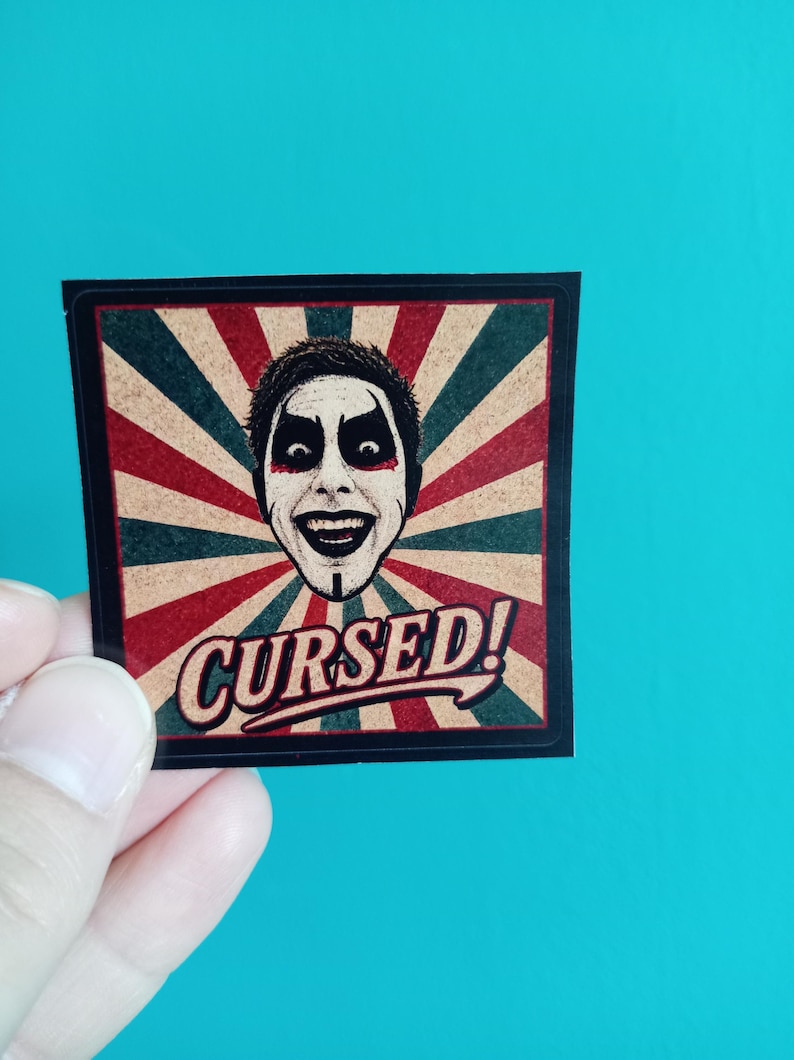 Peut inclure: Un autocollant carr&eacute; pr&eacute;sentant une illustration centrale d'une personne aux cheveux fonc&eacute;s avec un maquillage noir et rouge spectaculaire. Le fond se compose de rayons de soleil rouges et vert fonc&eacute;. Le mot CURSED! est imprim&eacute; en bas.