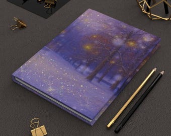May include: A hardcover journal with a winter landscape design. The cover features a purple and blue color scheme with a snowy scene and trees. Gold and black pencils and gold binder clips are also present.