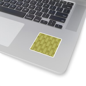 May include: A square sticker with a repeating pattern of olive green vertical stripes and arrow-like shapes. The sticker has a white border and is placed on a silver laptop.