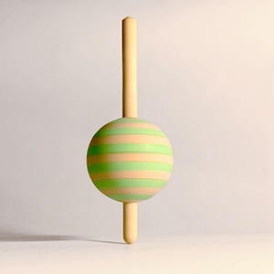 May include: A decorative bottle stopper with a spherical design. The sphere is striped with alternating bands of light green and peach. The stopper has a long, slender stem and a shorter stem at the bottom, all in a light beige color.