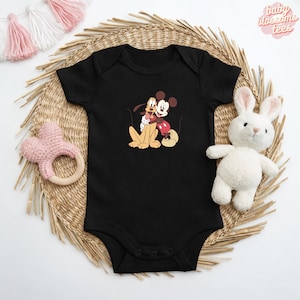 May include: Black baby bodysuit featuring a cartoon graphic of Mickey Mouse hugging Pluto. The bodysuit has short sleeves and snap closures. The text "baby blossoms tees" is in the upper right corner.