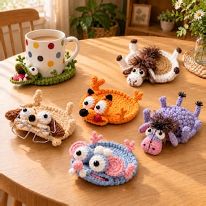 May include: A collection of five crocheted animal coasters featuring a dog with glasses, an orange fox, a purple donkey, a blue mouse, and a green alligator base under a white mug with colorful polka dots on a wooden table.