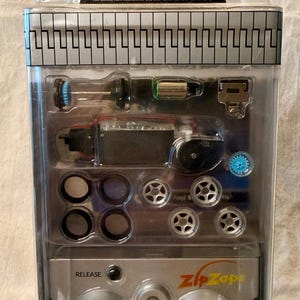 May include: A black Ford Mustang Cobra ZipZaps remote control car kit in original clear plastic packaging. Includes a miniature car, various silver wheels, tires, internal components, and a silver remote controller with 49MHz text and an on-off switch.
