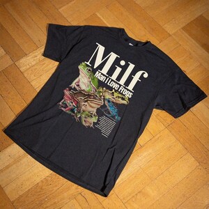 May include: Dark grey t-shirt with a colourful frog graphic and the text "Milf Man I Love Frogs" in white. The design features various frog species in shades of green, brown, pink, and blue.
