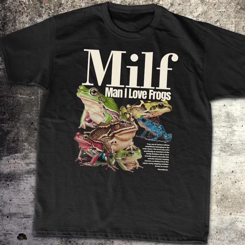 May include: Black t-shirt with a graphic of various colourful frogs. The text "Milf Man I Love Frogs" is printed in white above the frog illustration. The shirt has a crew neck and short sleeves.