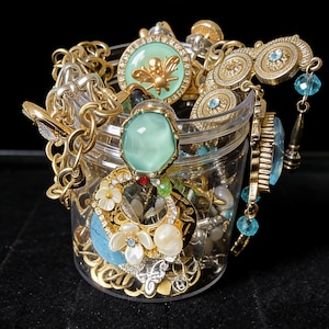 May include: A clear plastic jar overflowing with various pieces of jewelry. Gold and silver chains, pendants, and earrings are visible. Some pieces feature gemstones, pearls, and floral designs. A gold bee pendant is also visible.