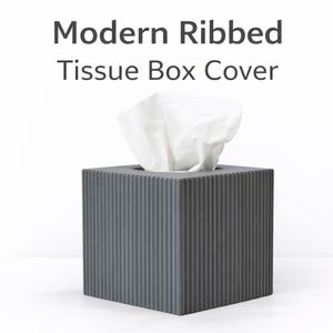 May include: A modern, gray ribbed tissue box cover with a square shape. White tissues are visible extending from the top opening. The text "Modern Ribbed Tissue Box Cover" is displayed above the box.