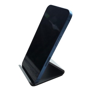 May include: A black smartphone is propped up on a foldable, angled stand. The phone has a dark screen and a blue frame. The stand is black and gray, designed to hold the phone at an angle for viewing.