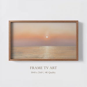 以下が含まれることがあります： 海上の夕日を描いた、額入りのデジタルアートプリント。オレンジ、ピンク、ゴールドの暖色系の色使いで、水面に太陽が反射しています。フレームは木製です。下部のテキストは「FRAME TV ART」と「3840 x 2160 | 4K Quality」です。