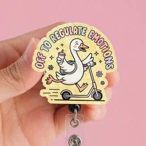 Peut inclure: Un enrouleur de badge avec un dessin d'oie en dessin animé sur un scooter, tenant une tasse de café. Le texte "Off to Regulate Emotions" est en arc-en-ciel. Le fond est doré avec des étoiles et des fleurs.