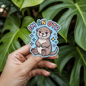 May include: A sticker featuring a cartoon otter with the text "I'm an OTR" in colorful letters. The otter is brown with a light blue background and surrounded by stars and hearts.
