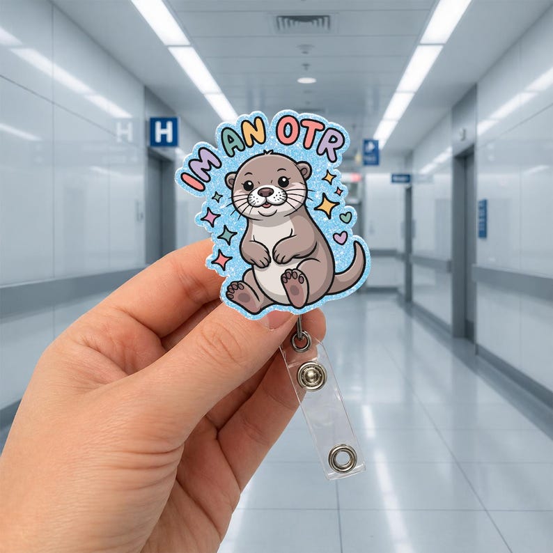 May include: A badge reel with a cartoon otter design. The otter is light brown with a white belly and is surrounded by blue stars and hearts. The text "I'm an OTR" is in a bubble around the otter.