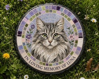 May include: A round stone memorial plaque featuring a mosaic-style portrait of a grey tabby cat. The cat is centered within a border of purple and green tiles, accented by small floral sprigs. The text IN LOVING MEMORY OF LUNA is printed below.