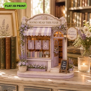 May include: A miniature bookstore model titled 'Violet's Bookshop' with a lavender and white color scheme. The facade features the text 'BOOKS READ THIS YEAR' above a display with the numbers 158, a small door, and a sign reading 'One More Chapter'.