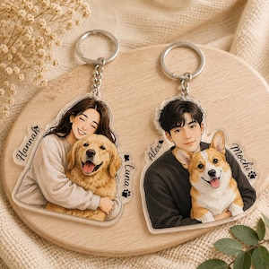 May include: Two clear acrylic keychains featuring custom illustrations. The left keychain shows a person named Hannah hugging a golden retriever named Luna. The right keychain shows a person named Alex holding a corgi named Mochi with paw prints.