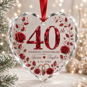 May include: A heart-shaped clear glass ornament featuring a red ribbon hanger. The design includes the text 40th WEDDING ANNIVERSARY, the names Jason and Taylor, the date 6.11.1986, two gold rings, and red rose floral accents with crystals.