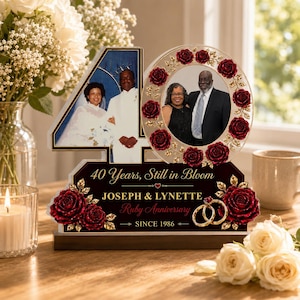 May include: A commemorative 40th anniversary plaque featuring a photo of a couple in a wedding dress and suit, a circular frame with red roses containing a photo of the couple, and the text 40 Years, Still in Bloom, JOSEPH & LYNETTE, Ruby Anniversary, SINCE 1986.