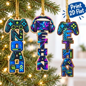 Op de afbeelding: Drie platte houten hangende ornamenten met gouden koordjes. Het linker ornament toont een gamecontroller en de naam NOAH. Het middelste ornament toont een koptelefoon en een monitor met de naam ETHAN. Het rechter ornament toont een gamecontroller en de naam ETHAN. Allemaal hebben ze blauwe, groene en paarse neon-graphics en de tekst Level 10.
