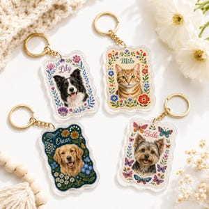 May include: Four rectangular acrylic keychains with gold-tone rings. Each features a pet portrait surrounded by floral illustrations and a name: Lily with a border collie, Milo with a tabby cat, Oscar with a golden retriever, and Belle with a terrier.