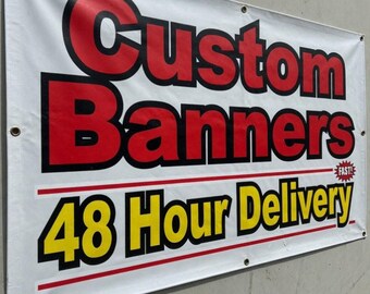 May include: White banner with the words "Custom Banners" in red and black lettering. Below, the text "48 Hour Delivery" is in yellow and black. The banner is hanging on a gray wall.