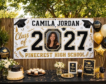 May include: A white graduation banner featuring the text CAMILA JORDAN, Class of 2027, and PINECREST HIGH SCHOOL in black and gold. The design includes a central photo of a person, black graduation caps, gold stars, and confetti graphics.