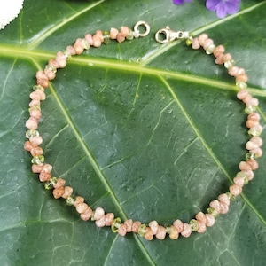 May include: A delicate bracelet made of small, faceted, pink and green gemstone beads. The bracelet is strung on a gold-toned chain and has a lobster clasp closure.