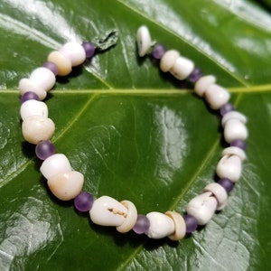 May include: A white and purple shell bead bracelet. The bracelet is made of small, white shell beads and purple glass beads.
