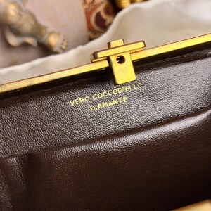 Peut inclure: Gros plan sur un sac &agrave; main en cuir marron avec un fermoir dor&eacute;. Le texte "VERO COCCODRILLO DIAMANTE" est estamp&eacute; en or sur le cuir. Le fermoir est rectangulaire avec un petit trou au centre.