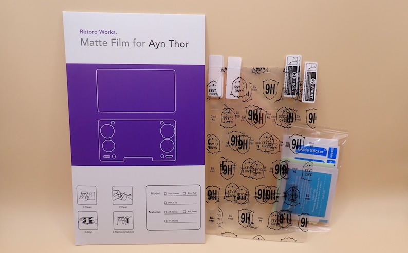 May include: A product package labeled "Retoro Works. Matte Film for Ayn Thor" with a purple and white design. The package includes a screen protector, cleaning wipes, and application tools. The screen protector has a 9H rating.