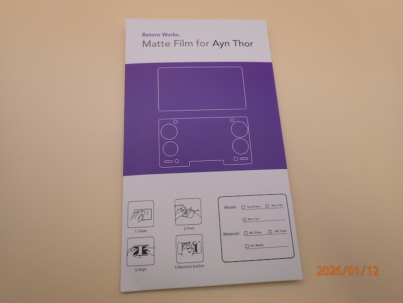 May include: A white and purple matte film sheet for the Ayn Thor handheld gaming device. The sheet features a diagram of the device and instructions for application. The text "Retoro Works. Matte Film for Ayn Thor" is visible.
