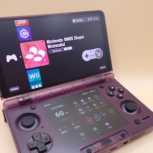 May include: A purple handheld gaming device with two screens. The top screen displays game icons, including "Nintendo SNES (Super Nintendo)". The bottom screen shows performance metrics. The device has buttons and a joystick for gameplay.
