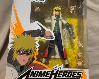 May include: A boxed Anime Heroes Namikaze Minato action figure from Naruto Shippuden. The figure is in a dynamic pose, with yellow hair and a white coat. The box features character art and the Anime Heroes logo.
