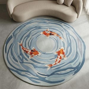 May include: A round rug featuring a koi pond design. The rug has a light blue background with darker blue wave patterns. Three orange and white koi fish are swimming in the pond. The rug is placed on a light-colored floor.