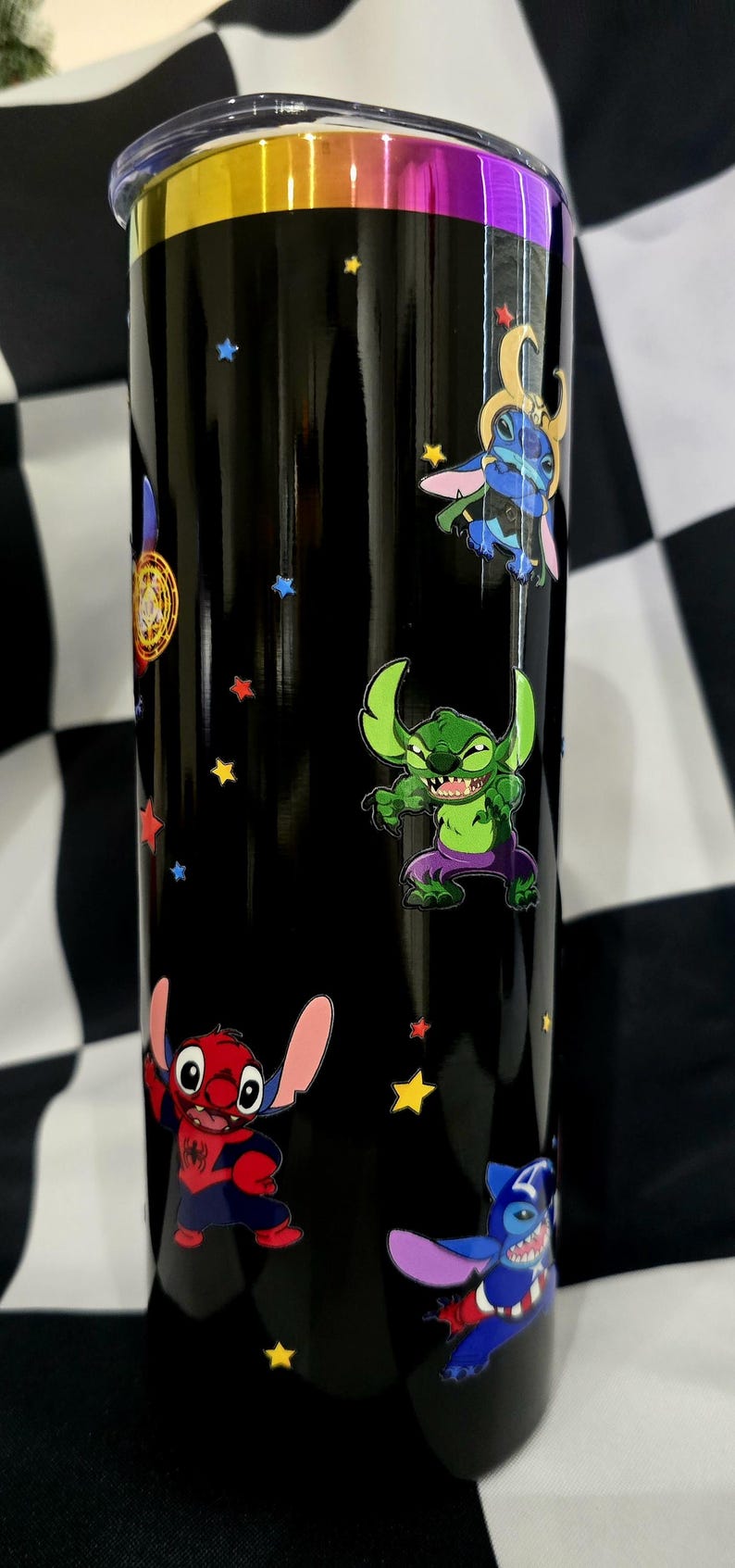 May include: Black tumbler featuring cartoon characters, including Stitch in various superhero-themed costumes, and colorful star accents. The tumbler has a metallic gold, purple, and yellow rim.