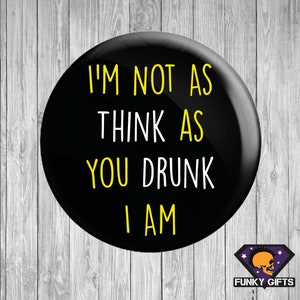 May include: A black circular badge with the words "I'M NOT AS THINK AS YOU DRUNK I AM" in yellow and white. The badge has a shiny surface and a logo in the bottom right corner.