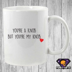 May include: White ceramic mug with the text "You're a knob but you're my knob" and a red heart.