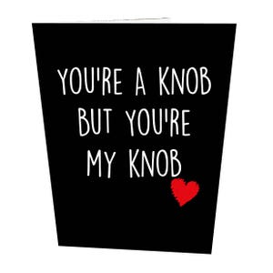 May include: A black greeting card with the text "YOU'RE A KNOB BUT YOU'RE MY KNOB" in white, and a small red heart. The card has a slightly angled design.