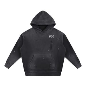 May include: A black distressed hoodie with a hood and a front pocket. The number "659" is printed in white on the upper chest. The fabric has a worn, faded look with white paint splatters, giving it a vintage feel.