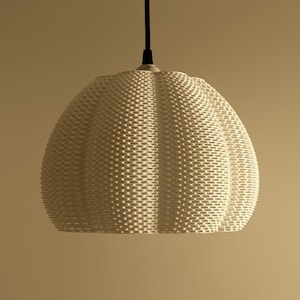 May include: Off-white pendant light fixture with a woven texture. The light has a rounded, bell-like shape and hangs from a black cord. The fixture is suspended against a neutral background.