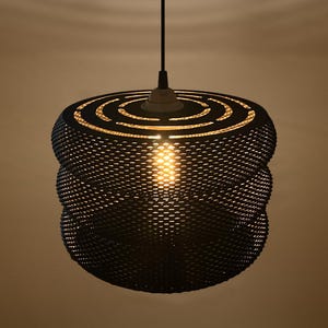 May include: A black pendant light fixture featuring a cylindrical, tiered shade with a fine mesh texture. The top of the shade has concentric circular cutouts, and a single warm light bulb is visible inside, casting a soft glow through the mesh.