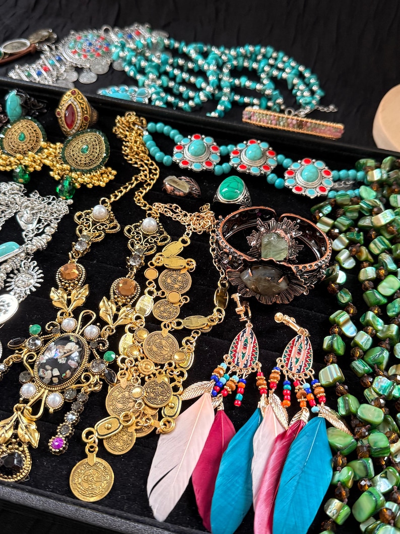 May include: A collection of bohemian jewelry including necklaces, earrings, rings, and bracelets. The jewelry features turquoise, gold, and silver tones, with accents of red, pink, and blue. Some earrings have feather details.