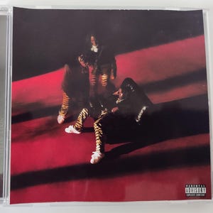 Könnte beinhalten: CD-Hülle mit Albumcover, das drei Figuren auf rotem Grund zeigt. Die Figuren tragen dunkle Kleidung und gemusterte Hosen. Der Albumtitel lautet "Life of a Don". Ein Warnhinweis für Eltern ist vorhanden.