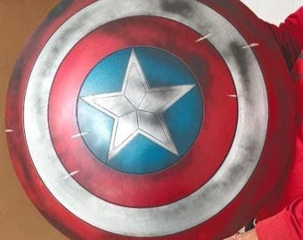 May include: A circular shield featuring a central blue circle with a large white five-pointed star, surrounded by alternating red and silver rings. The surface has a weathered, distressed finish with dark shading and light scratch marks.