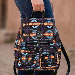 May include: A black backpack with a Southwestern-inspired geometric pattern in shades of orange, blue, and purple. The backpack has two front pockets, a top handle, and adjustable straps. The flap closure is secured with a metal clasp.
