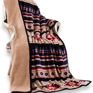 May include: A beige and patterned blanket draped over a chair. The blanket features a geometric design in navy blue, red, and black stripes and shapes. The reverse side is a soft, plush beige material. The blanket is a cozy home decor item.