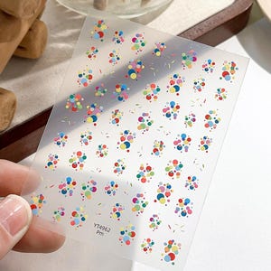 Op de afbeelding: Transparante nagelkunststickers met een patroon van kleurrijke stippen en kleine streepjes. De stippen zijn in verschillende kleuren, waaronder rood, blauw, geel en groen. De tekst "YT4962 PM" is gedrukt.