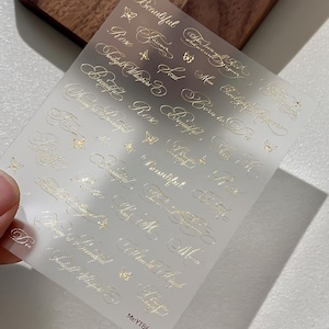 May include: A translucent sticker sheet featuring gold foil calligraphy text and small butterfly icons. The text includes phrases like Beautiful, Rose, Twilight Whispers, Soul, and Born to Die. The sheet is marked with the code MeYT86 at the bottom.