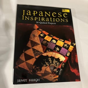 May include: A book titled "Japanese Inspirations" with 18 quilted projects. The cover features a close-up of a quilted fan and pillow in shades of orange, gold, purple, and black. The author's name, Janet Haigh, is printed at the bottom.