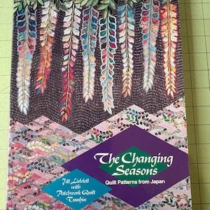 May include: A book cover featuring a colorful quilt design with cascading floral patterns in shades of red, orange, blue, and green. The title "The Changing Seasons" is displayed in white and green text, with the subtitle "Quilt Patterns from Japan".